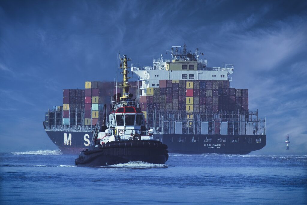 A tugboat guiding a container ship into port.