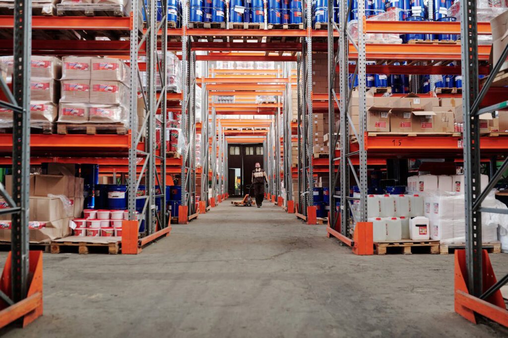 Aisle in a warehouse with a man pulling a pallet jack in the distance. 